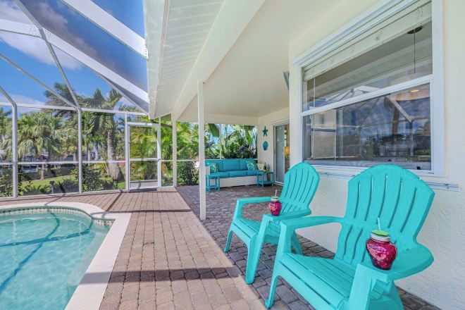 A covered outdoor area with a pool, two chairs, and a bench.