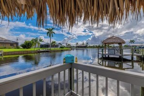 A waterfront view with a thatched-roof structure, a pool, and a small boat dock. - Villa Barefoot Cove (Cape Coral)