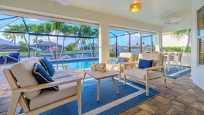 A poolside area with lounge chairs, a table, and a view of a pool and palm trees. - Villa Barefoot Cove (Cape Coral)