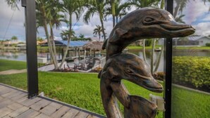 A sculpture of two stylized bird heads, a paved walkway, and a view of a landscaped area with palm trees and a body of water. - Villa Barefoot Cove (Cape Coral)