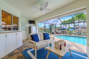 Zona junto a la piscina con un sofá, una mesa con bebidas y vistas a la piscina y al espacio exterior.