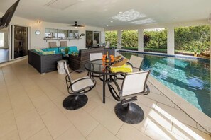 Un área de piscina interior moderna con una mesa de comedor y sillas, un sofá y un ventanal con vistas a zonas verdes.
