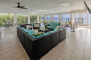 A spacious indoor area with a large wicker sofa, a dining table, and a view of the sea. - SeaBreeze Vista (Cape Coral)