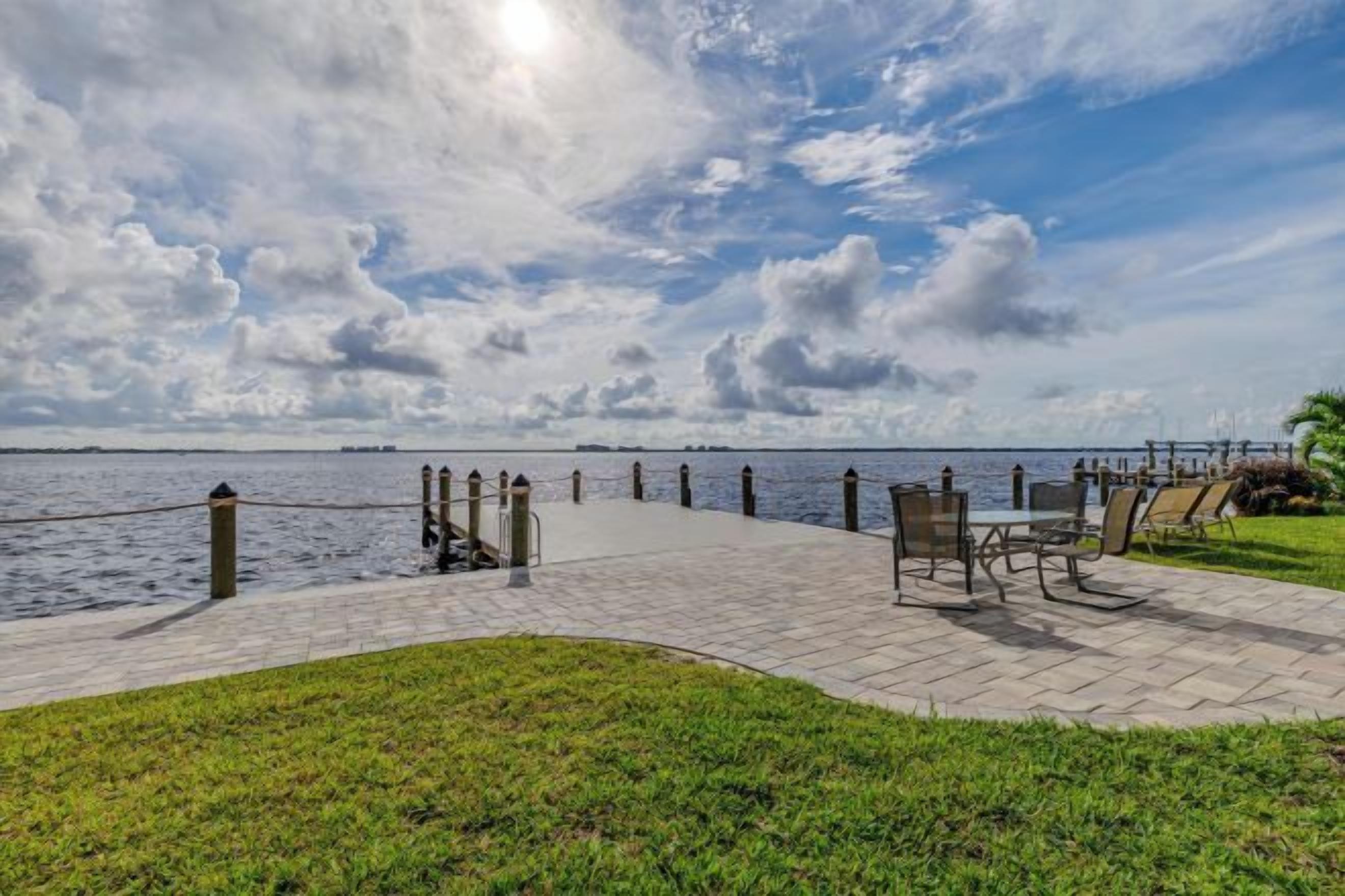 A paved walkway leading to a body of water, with benches and a railing along the edge.