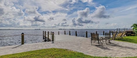 A paved walkway leading to a body of water, with benches and a railing along the edge.