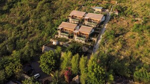 A hillside property with multiple buildings, including a main house and guest accommodations, surrounded by lush greenery and a mountain in the background.