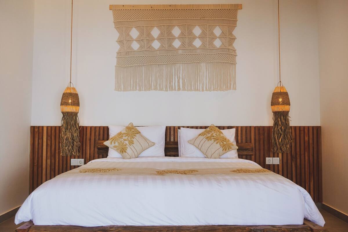 A bed with a wooden headboard, two hanging lamps, and a woven tapestry on the wall.