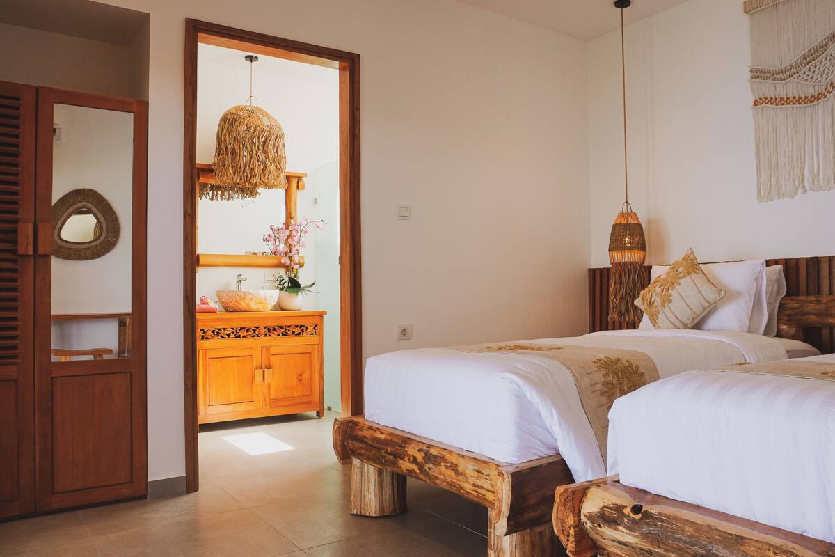 A bedroom with two wooden beds, a wooden nightstand, a wooden dresser, a mirror, and a hanging light fixture.