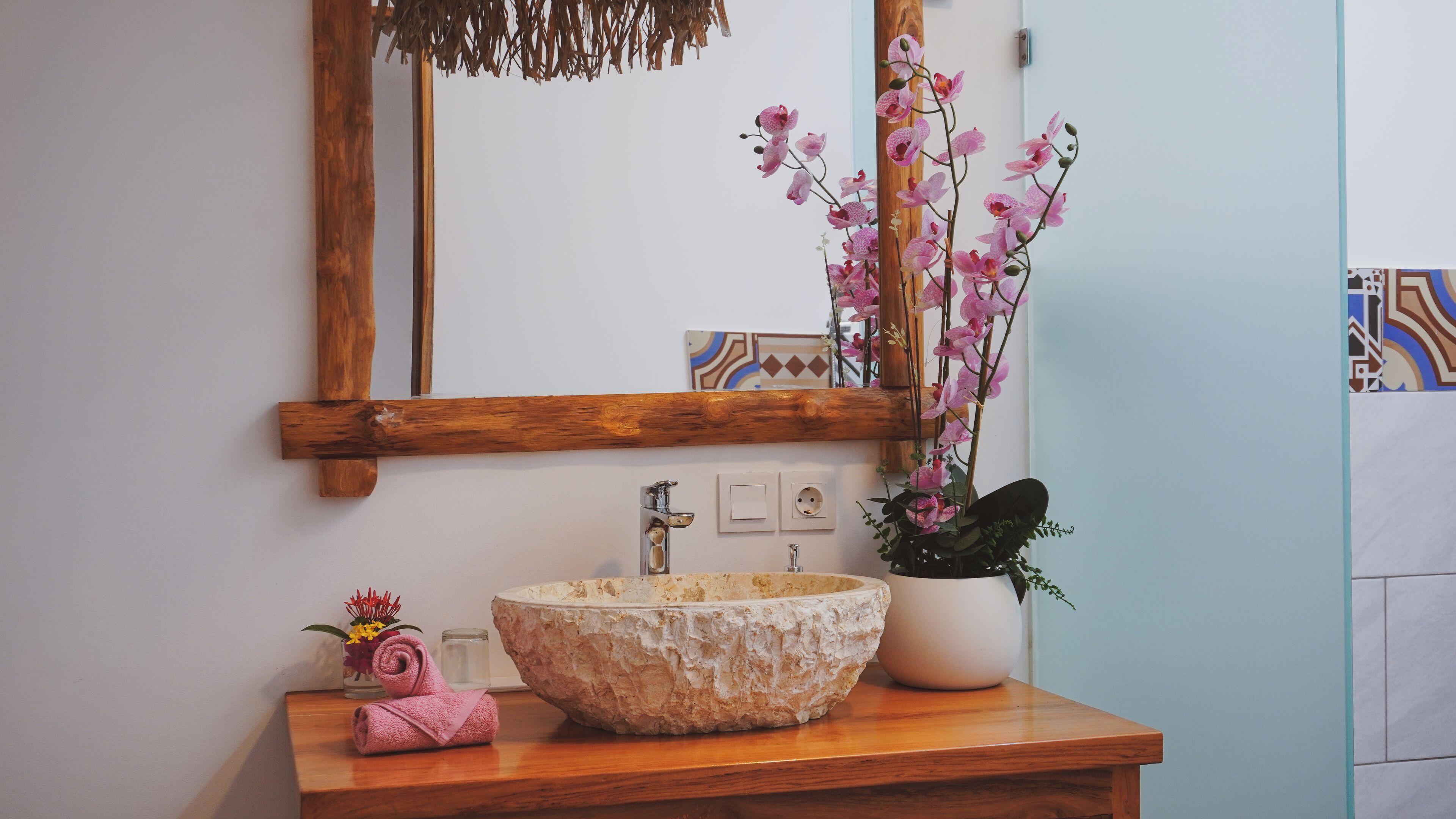 A bathroom with a wooden vanity, a large bowl sink, a mirror, and a potted orchid plant.