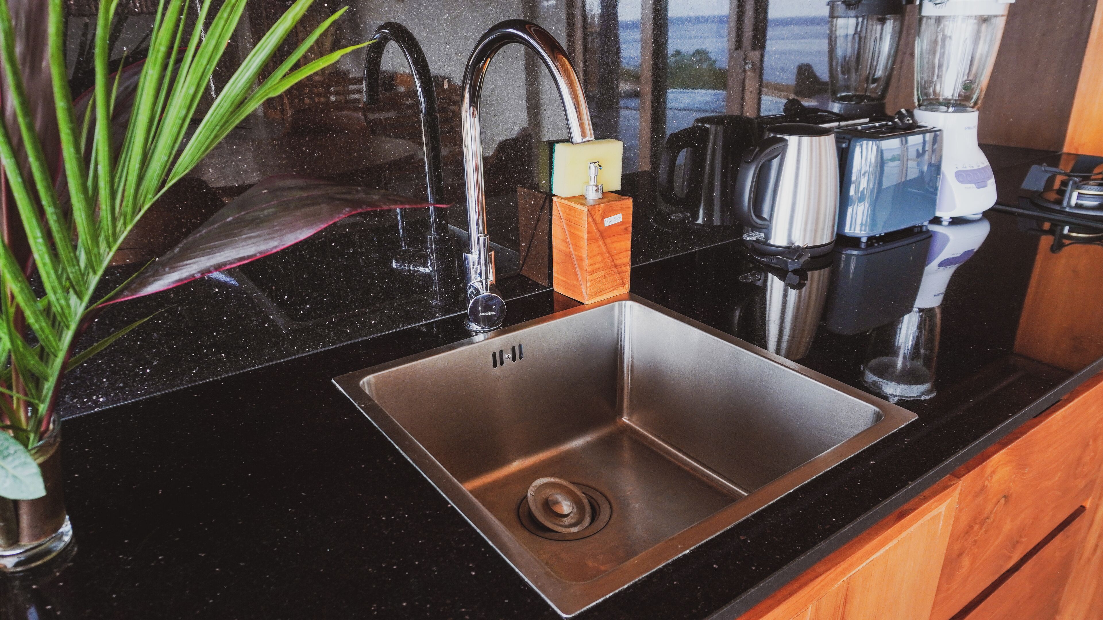 A kitchen with a stainless steel sink, a coffee maker, and a kettle on the counter.