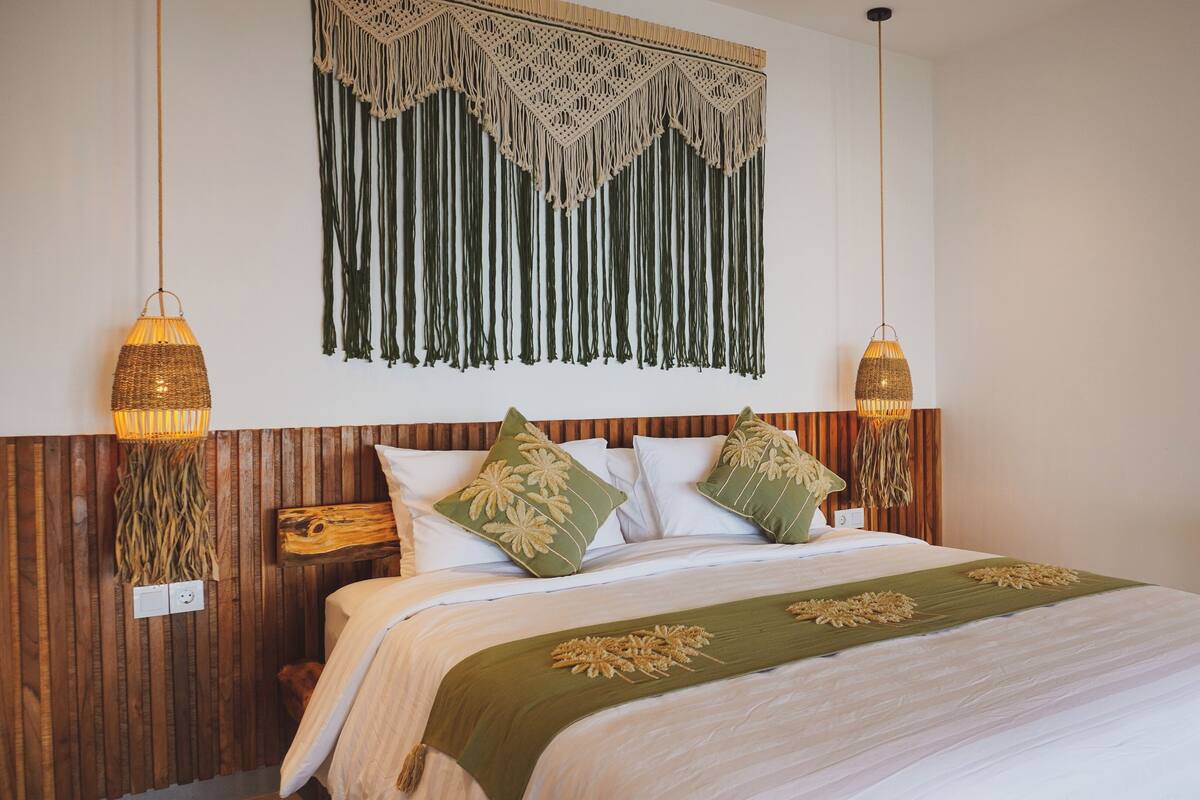 A bed with a wooden headboard, two bedside lamps, and a macramé wall hanging.