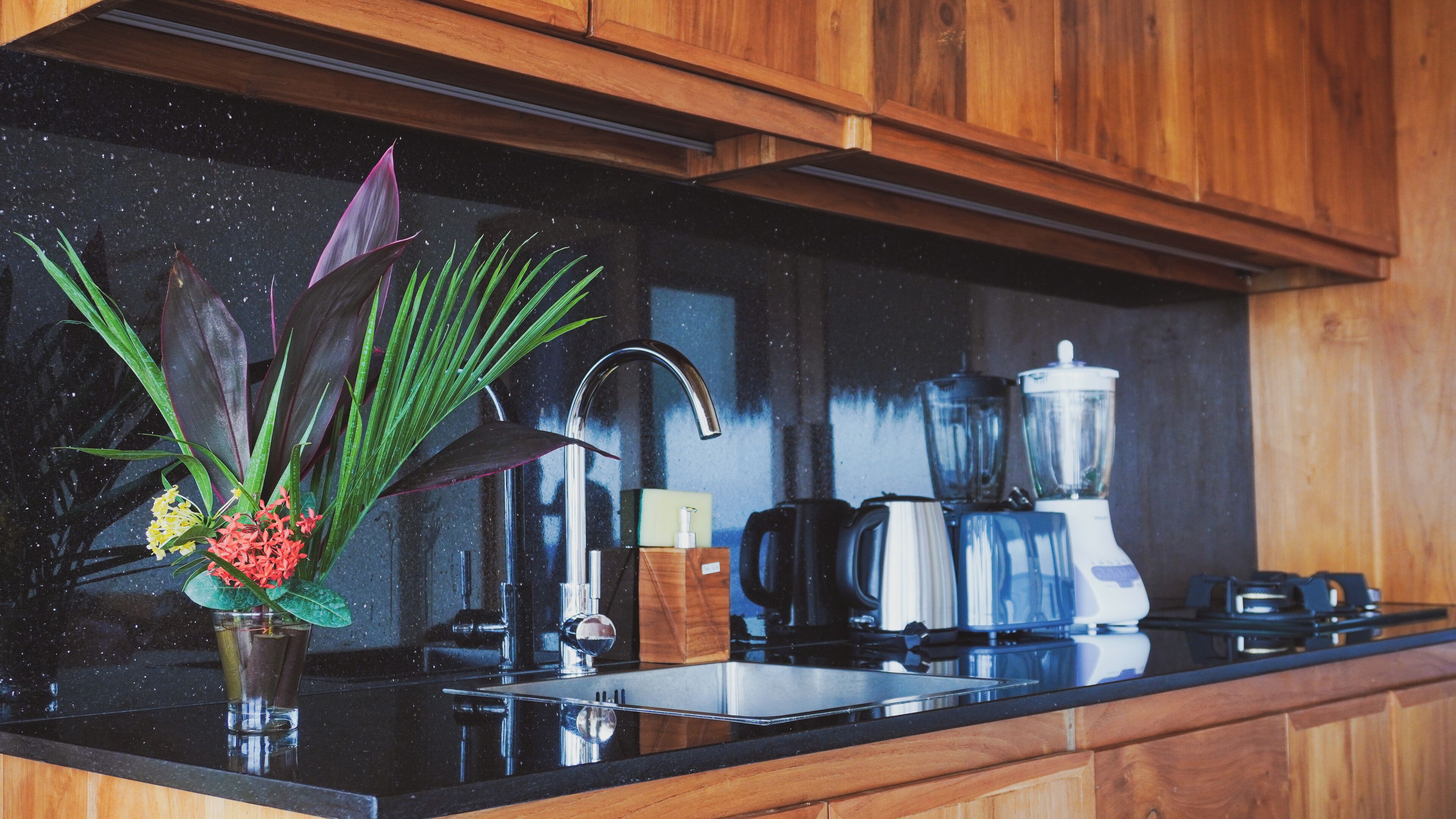 A kitchen with wooden cabinets, a black countertop, a sink, a faucet, a blender, and a coffee maker.