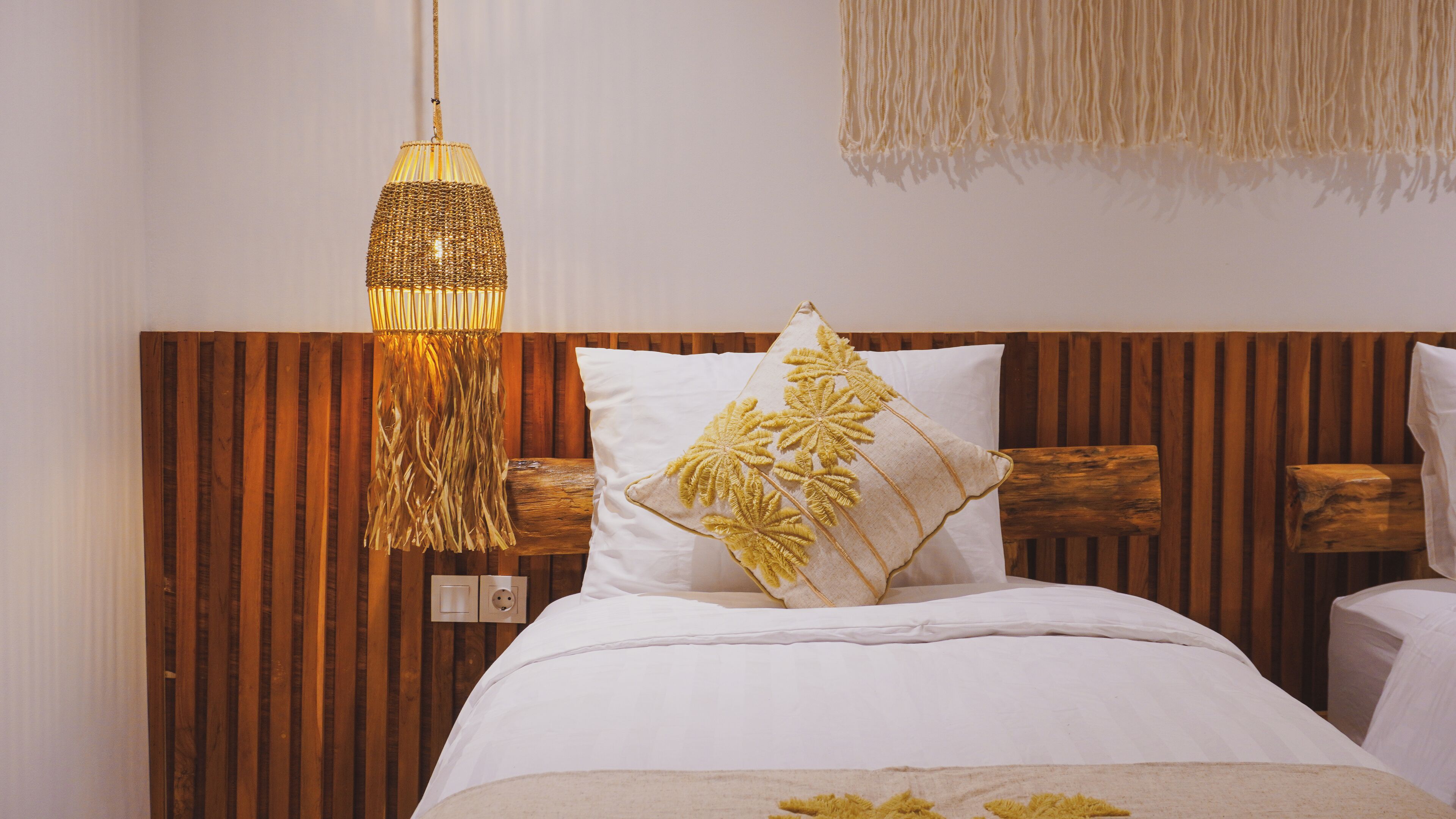Une chambre à coucher avec une tête de lit en bois, du linge de lit blanc et un luminaire suspendu.