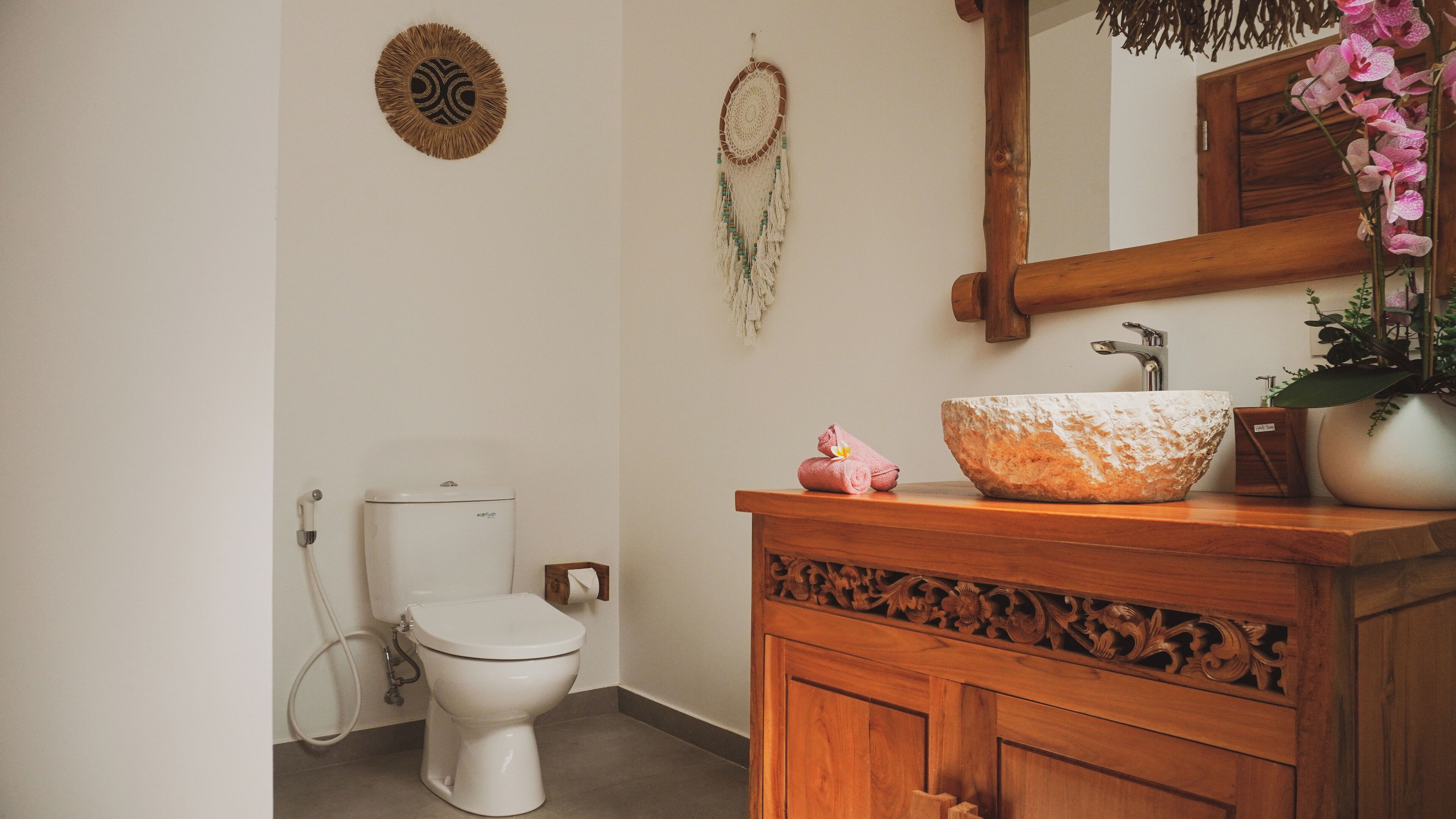 Une salle de bain avec des toilettes blanches, un meuble-lavabo en bois doté d’un grand évier en pierre et un miroir au-dessus du meuble-lavabo.