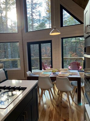 Een moderne keuken met grote ramen, houten vloeren en een eethoek met stoelen en een tafel voor vier personen.
