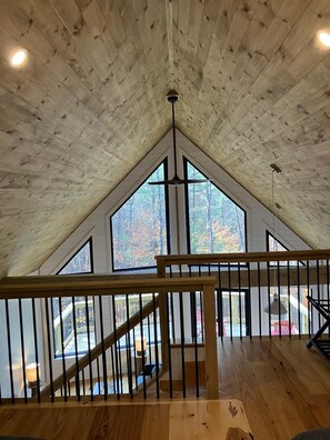 A spacious attic room with a sloped ceiling, large windows, and a wooden staircase. - Modern Cabin 3bedroom 2bathroom- Whiteface Adirondacks (Jay)
