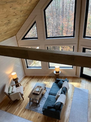 A cozy loft bedroom with a sloped ceiling, large windows, a wooden floor, a sofa, a chair, and two floor lamps. - Modern Cabin 3bedroom 2bathroom- Whiteface Adirondacks (Jay)
