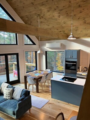 A modern kitchen with a central island, large windows, and a dining area with a view of the outdoors. - Modern Cabin 3bedroom 2bathroom- Whiteface Adirondacks (Jay)