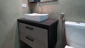 Et moderne badeværelse med en hvid vask, mørkt skab og toilet.