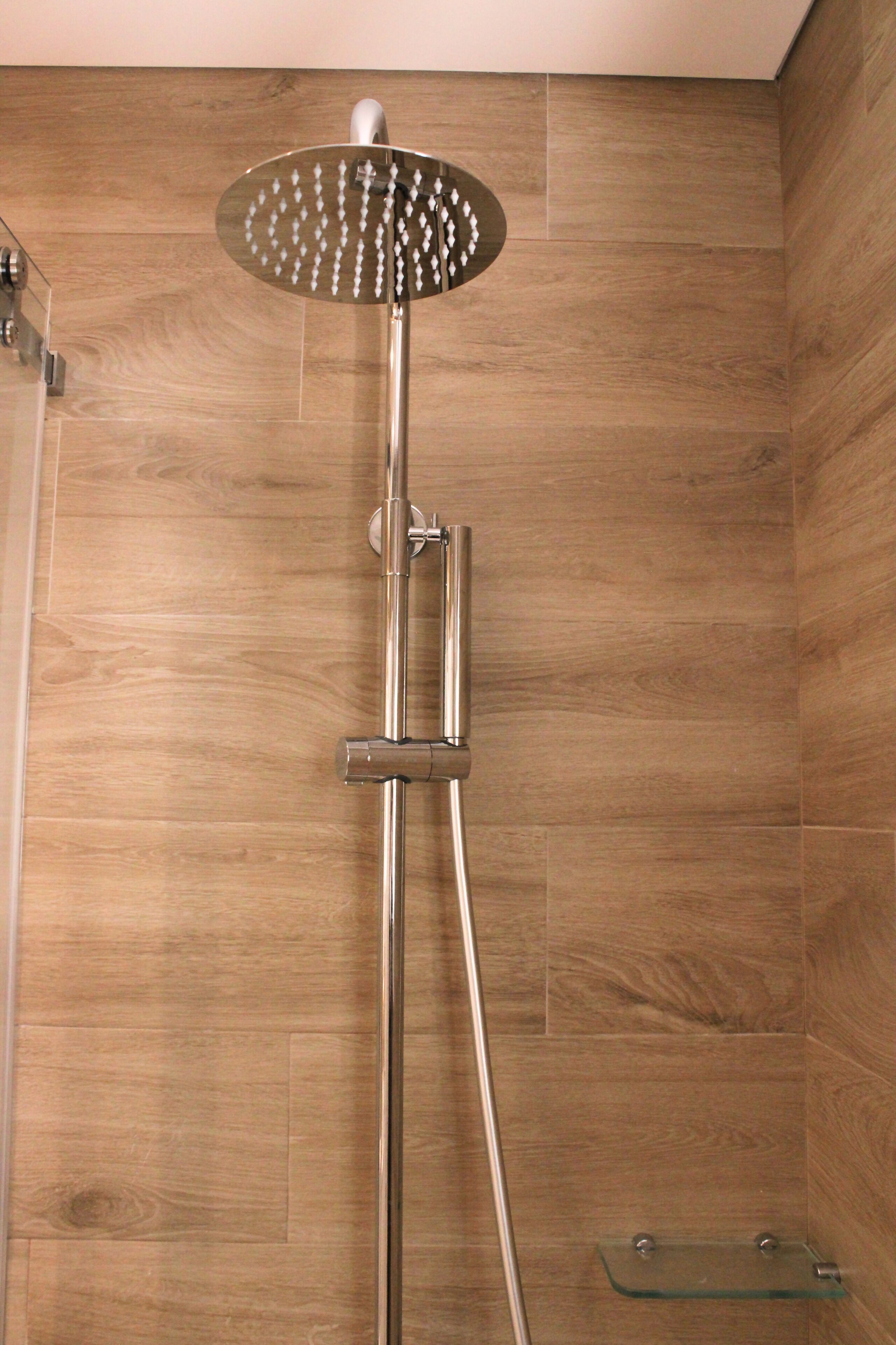 A shower with a modern design, featuring a rain shower head and a glass shelf.