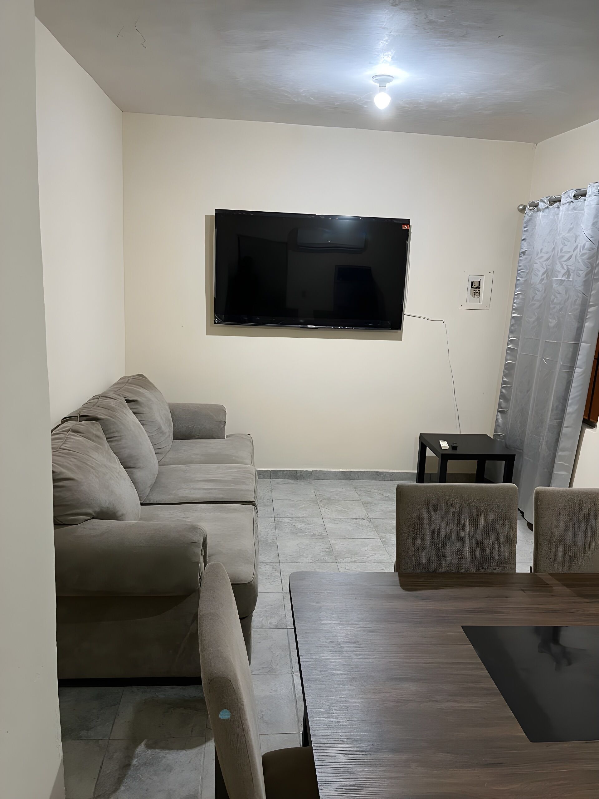 Een woonkamer met een flatscreen televisie aan de muur, een grijze bank, een houten salontafel en een klein zwart bijzettafeltje.