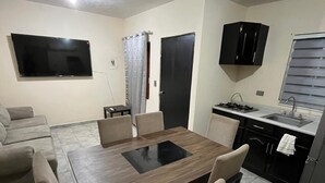 Un espace de vie compact comprenant un coin repas, une kitchenette et un téléviseur fixé au mur.