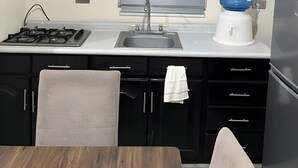A compact kitchen with black cabinets, a gas stove, a sink, a window with blinds, and a water dispenser. - Spacious, centrally located house near Laguna del Náinari (Ciudad Obregón)