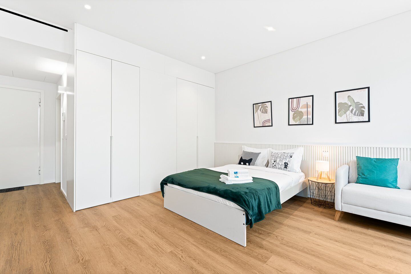 Una camera da letto moderna con un letto, un'armadio bianco e un comodino con una lampada.