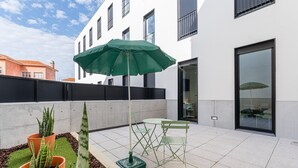 A patio area with a table and chairs, a green umbrella, and potted plants. - GuestReady – Magnolia (Aveiro)