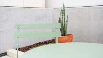 A light green chair with a metal frame and a potted plant in the background.