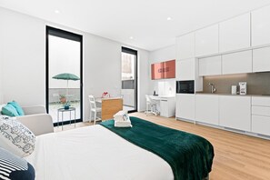 Une chambre d’hôtel moderne équipée d’un lit, d’un bureau, d’une chaise, d’une petite table avec un parapluie et d’un coin cuisine.