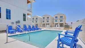 A swimming pool area with blue chairs and a pool ladder, surrounded by white buildings with balconies. - Beach Side Home, Steps from the Sand. Ocean Edge 14 New Build 2025 (Orange Beach)