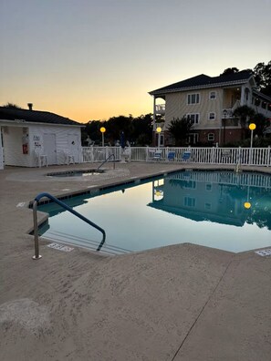 A swimming pool with a white fence, a lifeguard stand, and a building in the background. - Riverwalk 3BR Condo | Fairways & Flip‑Flops, First Floor Near Beach & Golf (Myrtle Beach)