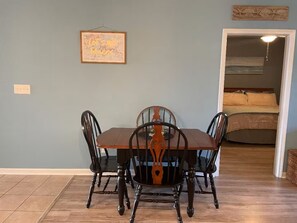 A dining area with a wooden table and chairs, a framed map on the wall, and a bedroom visible through an open door. - Riverwalk 3BR Condo | Fairways & Flip‑Flops, First Floor Near Beach & Golf (Myrtle Beach)