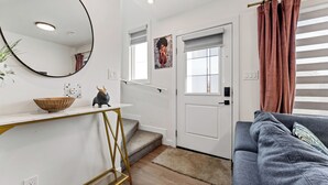 A modern living room with a grey sofa, a round mirror, a white door, and a staircase leading to another room. - Morden Garden Suite With Parking (Edmonton)