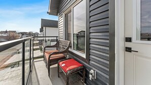 A balcony with wicker furniture and a red cushion, overlooking a residential area. - Morden Garden Suite With Parking (Edmonton)