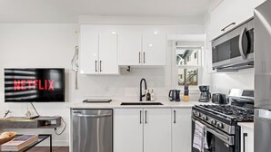 A modern kitchen with white cabinets, a stainless steel dishwasher, a black stove, and a microwave. - Morden Garden Suite With Parking (Edmonton)