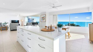 Un salón moderno con una isla grande, un televisor y un comedor con vistas al océano.