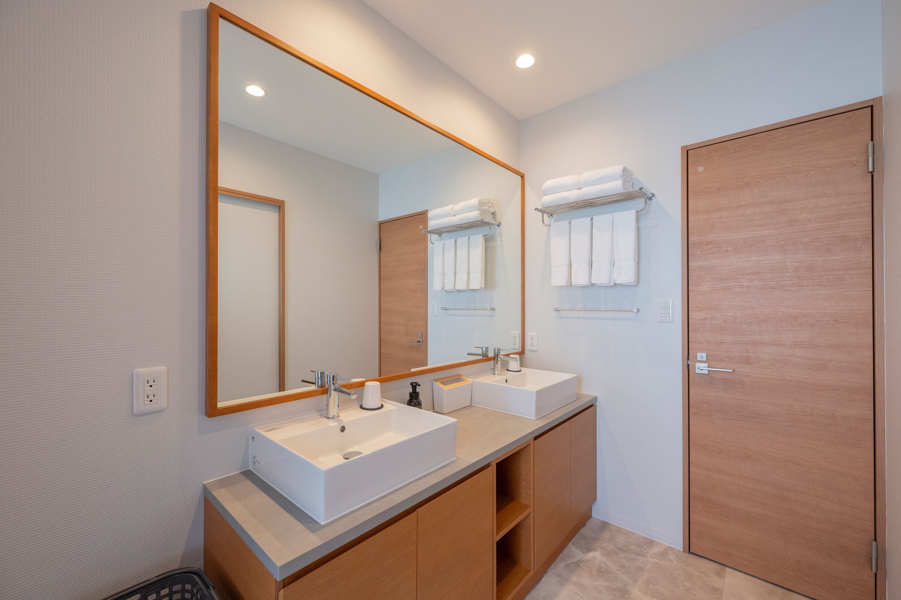 A modern bathroom with two sinks, a large mirror, and a wooden door.