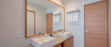 A modern bathroom with two sinks, a large mirror, and a wooden door.