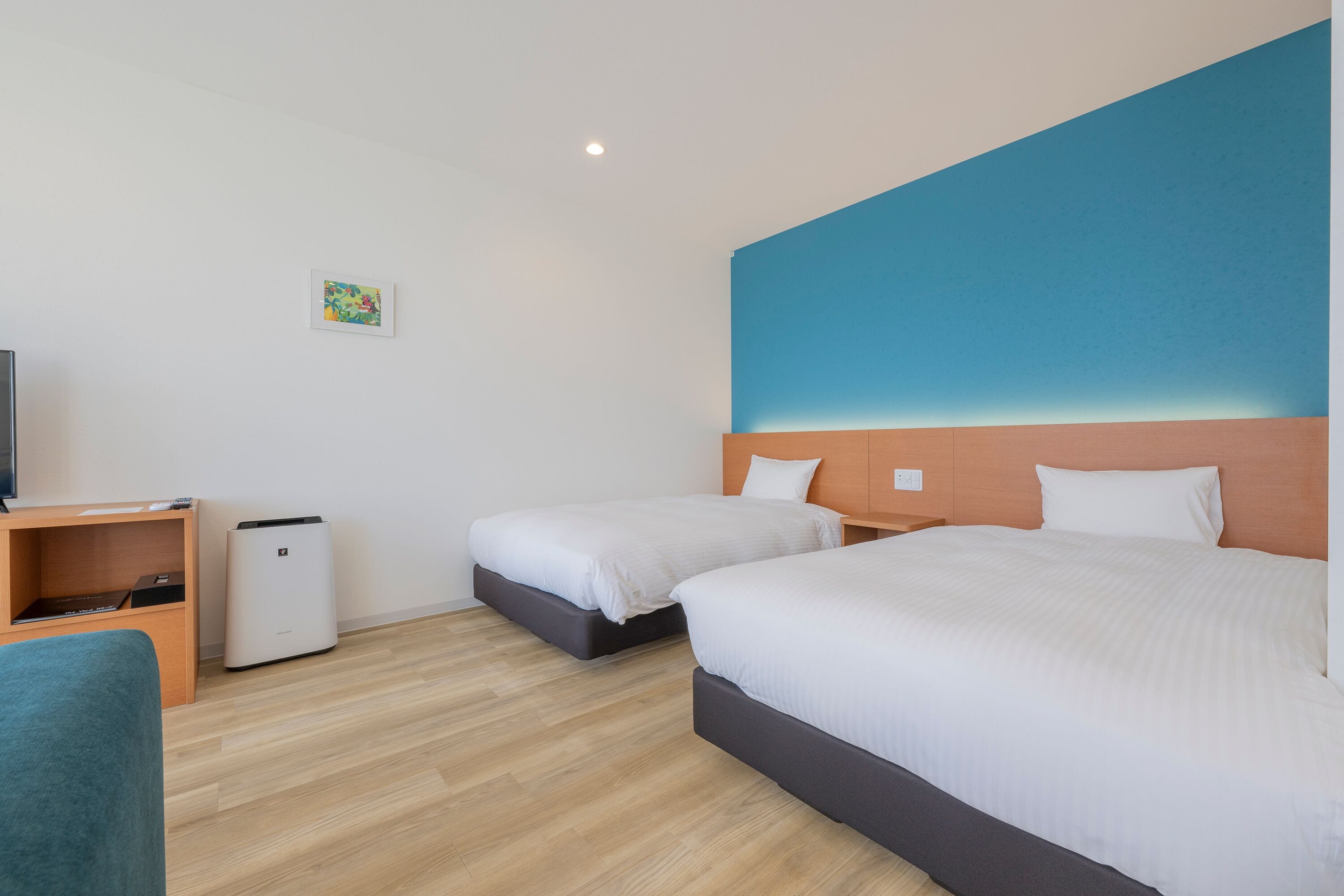 A hotel room with two beds, a desk, a chair, and a small TV.