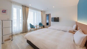 Quarto de hotel com duas camas, televisão, escrivaninha com cadeiras e janela com cortinas.