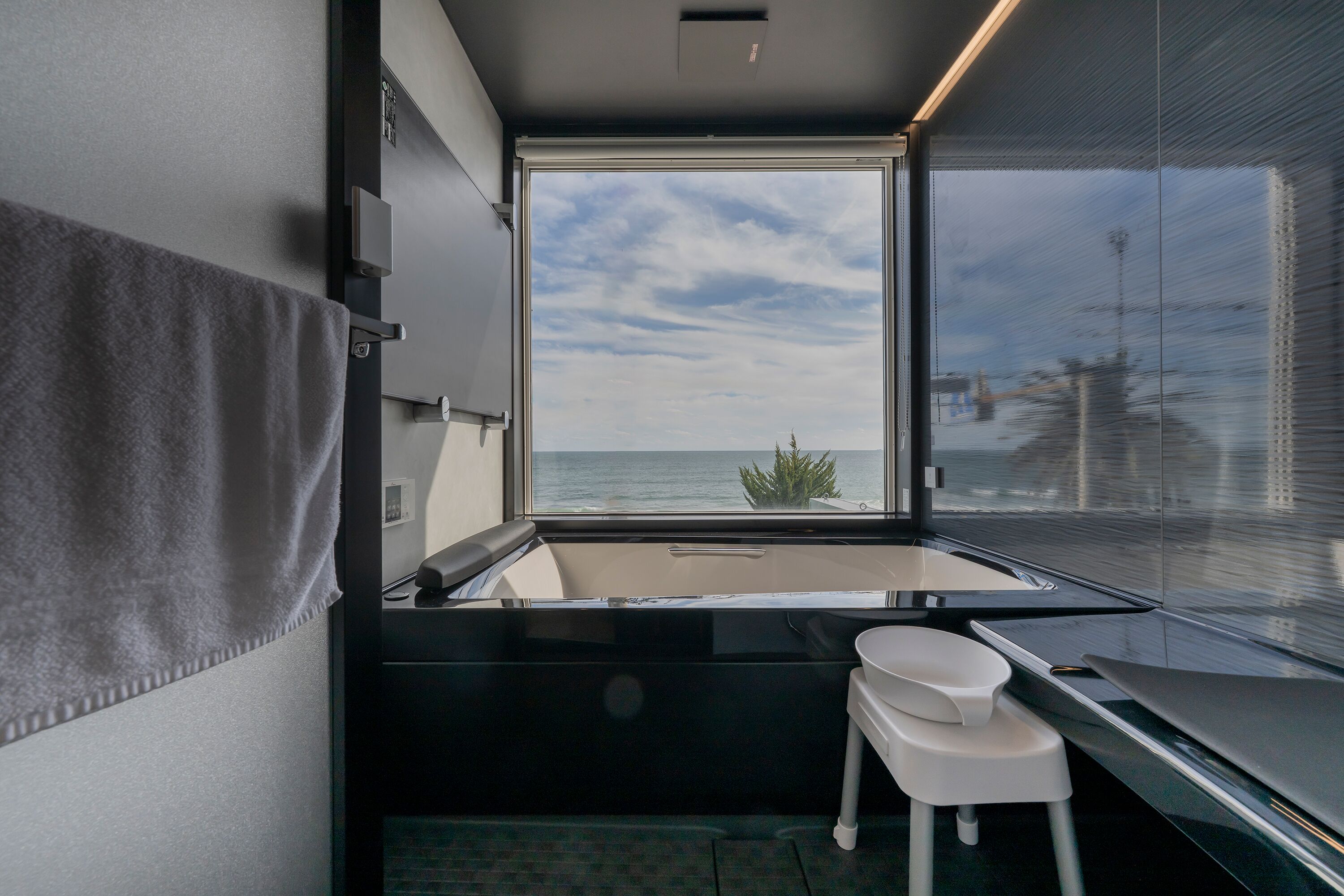 A modern bathroom with a large window, a bathtub, and a small stool.