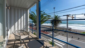 Uma varanda com móveis de vime, vista para a praia e uma rua com palmeiras.