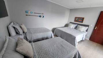 Un dormitorio con dos camas, un televisor montado en la pared y una puerta.