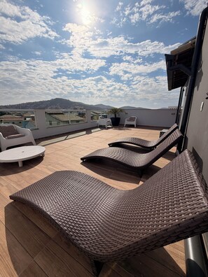 A rooftop terrace with wicker lounge chairs, a potted plant, and a view of the cityscape. - Canoa dos Anjos Suites (Arraial do Cabo)
