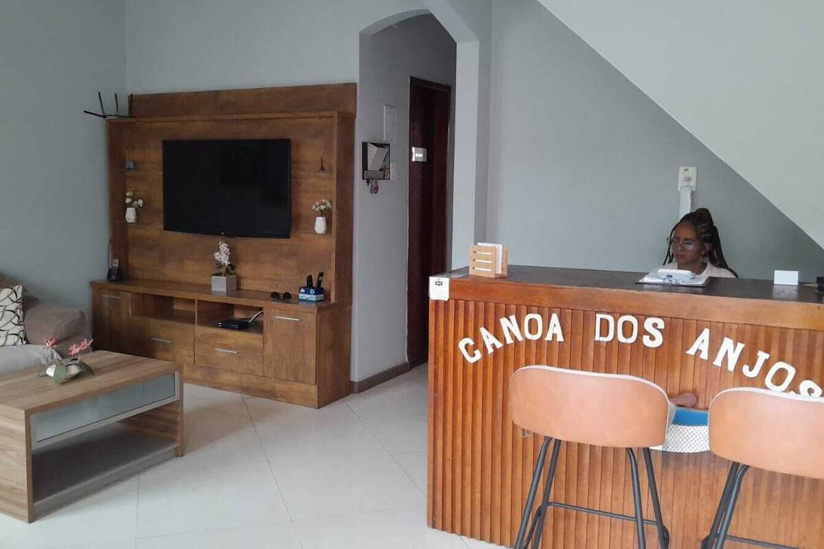 Un salon équipé d’un téléviseur, d’un meuble de rangement en bois et d’un coin bar portant l’inscription « CANOA DOS ANJOS ».