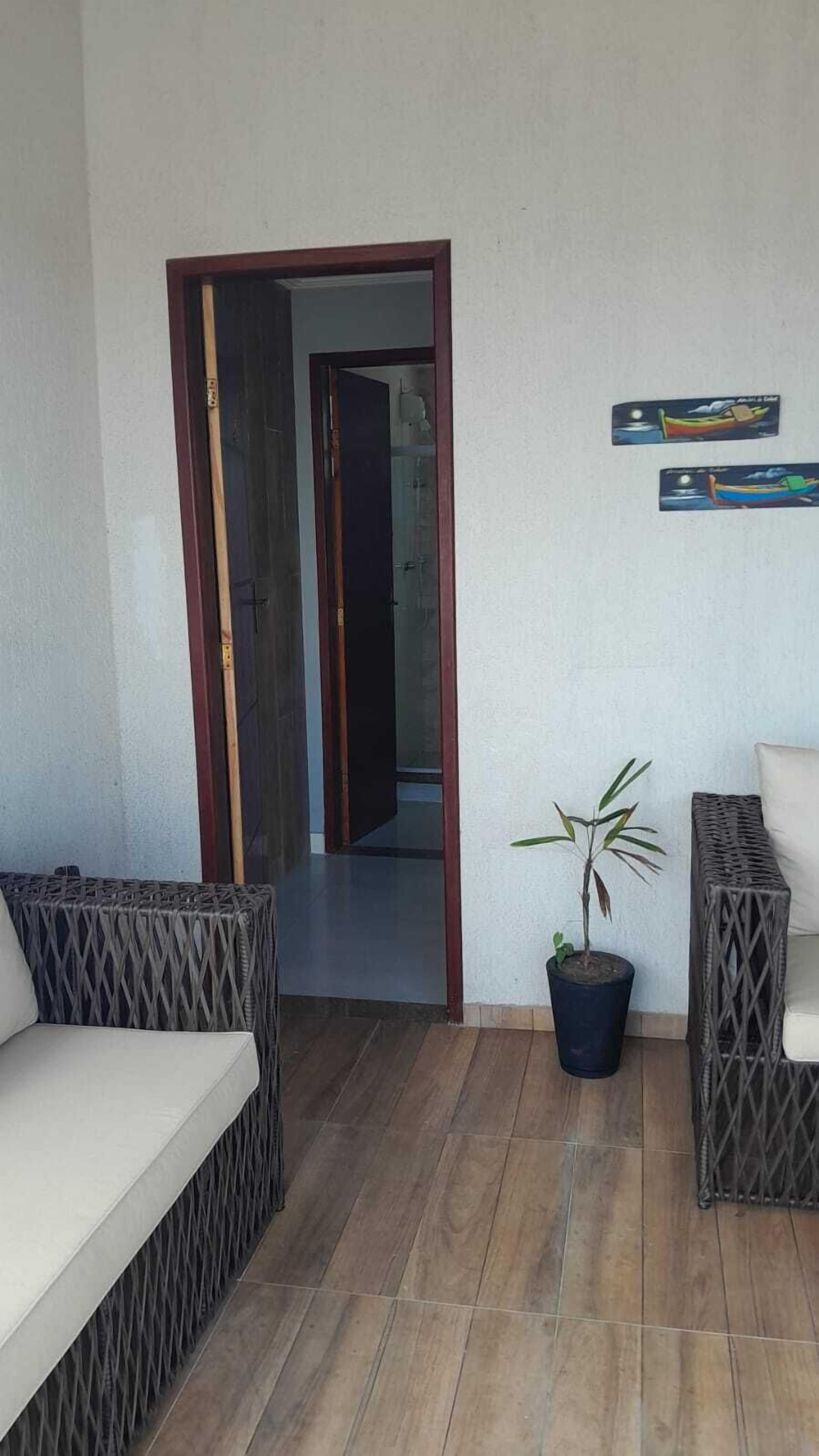 A room with a wooden floor, a potted plant, and two wicker sofas.