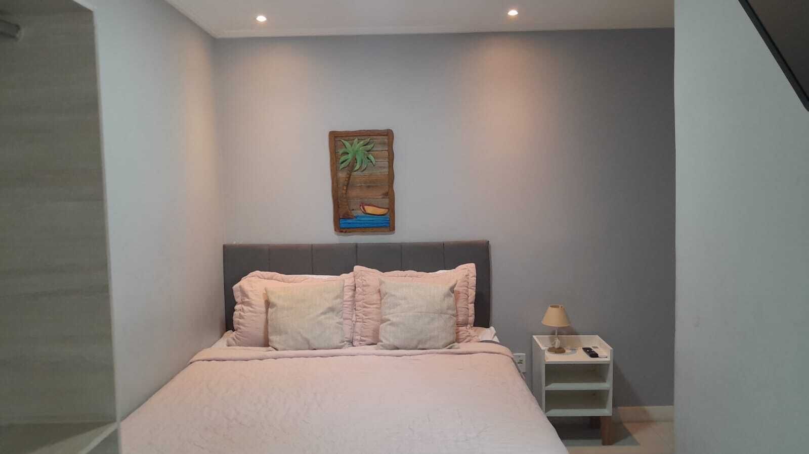 Un dormitorio con cama, mesita de noche, lámpara y una obra de arte en la pared.