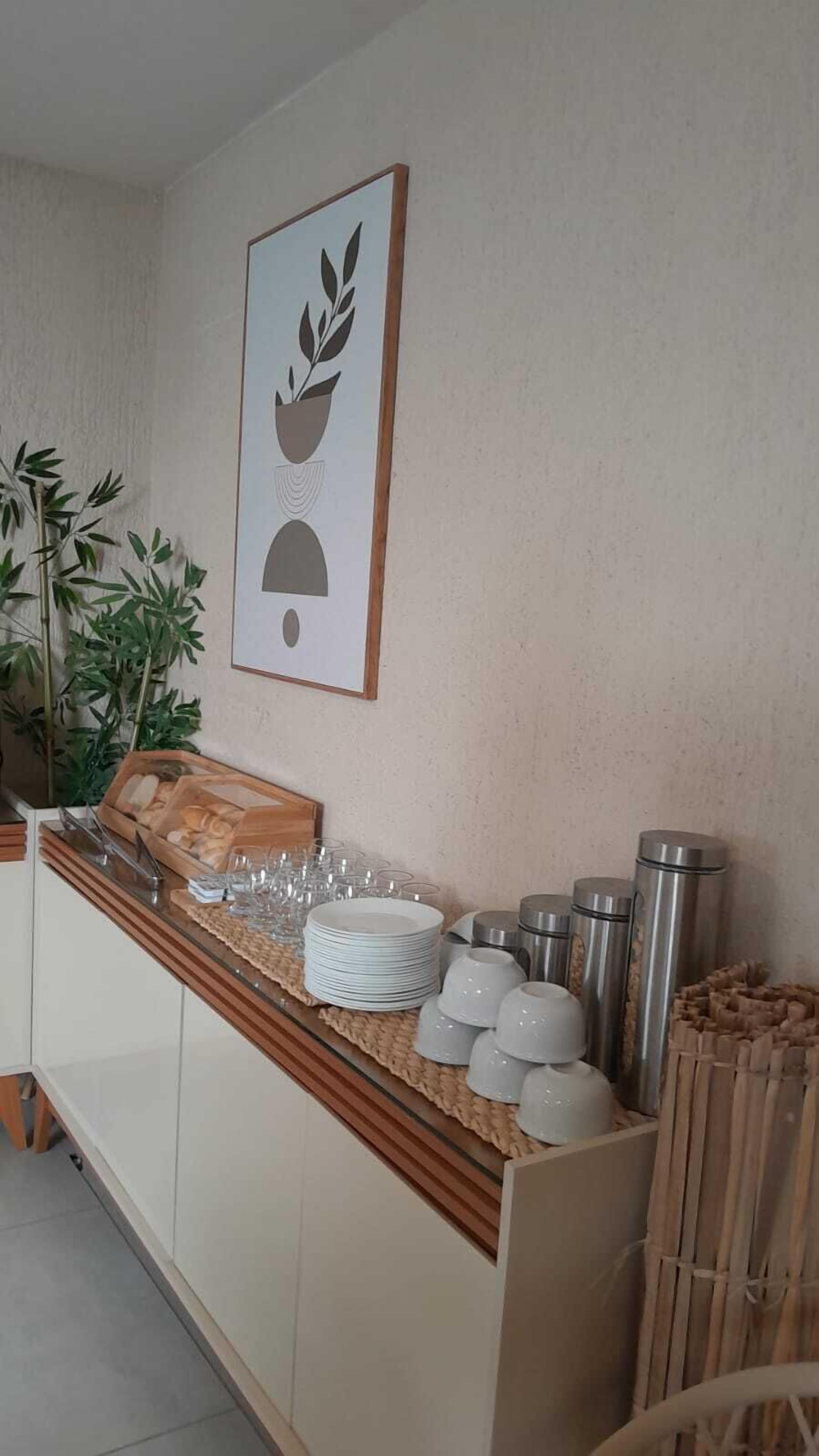 A kitchen area with a wooden countertop, a potted plant, and various kitchenware including plates, cups, and a kettle.
